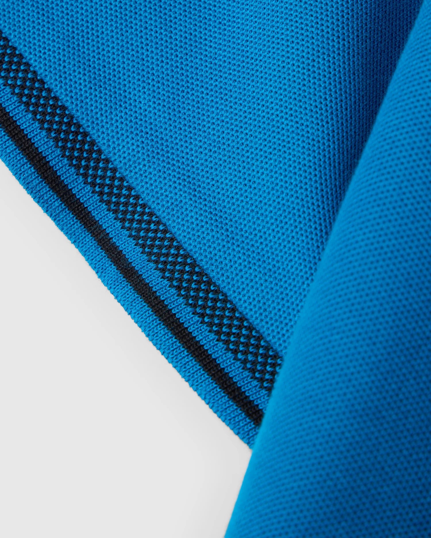 Close-up of the corner of a bright blue Pima cotton piqué fabric with a textured weave from the KIDS MALTON PIQUE POLO SHIRT - B0K950D200 by Psycho Bunny. The edge is accented with a black stripe running parallel to the fabric's border. The fabric shows a folded corner, displaying both the front and reverse sides, reminiscent of a classic Malton polo.