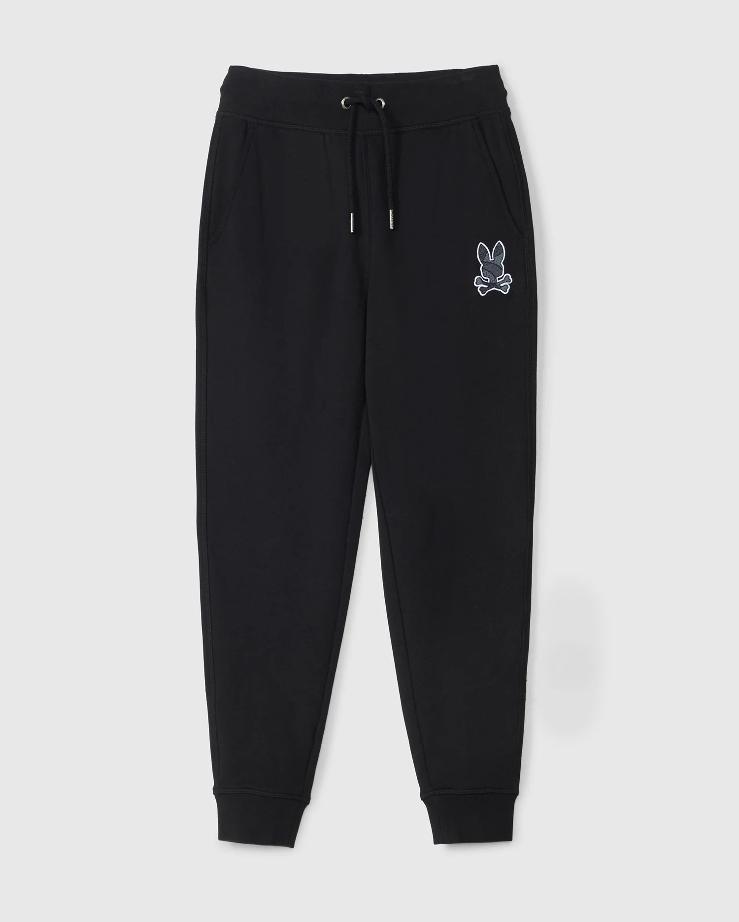 The KIDS LENOX REGULAR FIT SWEATPANT by Psycho Bunny is a pair of black jogger pants with an elastic waistband, drawstring, and ribbed ankle cuffs. These kids' sweatpants also feature a white embroidered graphic of a rabbit head above crossed bones on the left pocket.