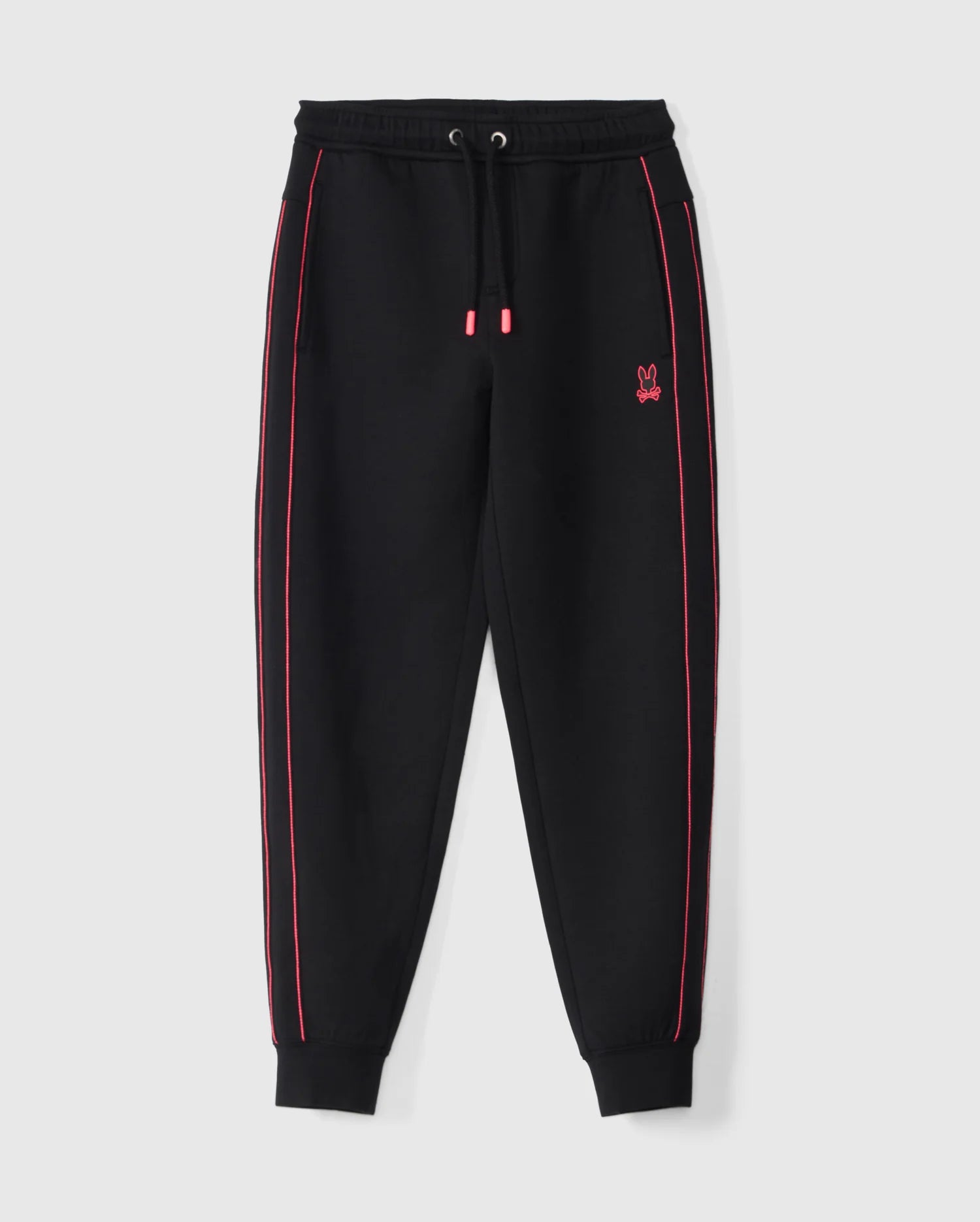 The Psycho Bunny KIDS TRAVIS TRACK PANT - B0P143D200 features black elastic and comfortable kids' track pants with a drawstring waist and red accents, including contrast chainstitch stripes along the sides and red-tipped drawstrings. A small red bunny logo is embroidered on the left thigh. The cuffs and waistband are elasticated, presented against a white background.