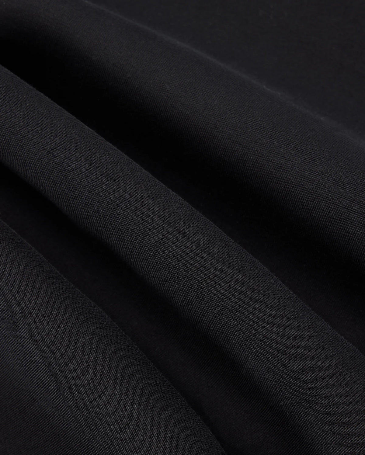 Close-up image of the black fabric with fine, parallel ribbing showcasing its texture. The fabric exhibits slight waves due to gentle folds, reminiscent of the subtle detail found in the high-quality KIDS TRAVIS TRACK PANT - B0P143D200 by Psycho Bunny, which is both elastic and comfortable.
