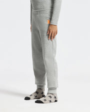 A person wearing Psycho Bunny's KIDS VAL WAFFLE PANT - B0P673E200 in light gray, matched with a coordinating long-sleeve shirt. They have one hand resting on their side. Gray socks featuring black patterns and black toe caps complete the look as they stand against a plain white background.