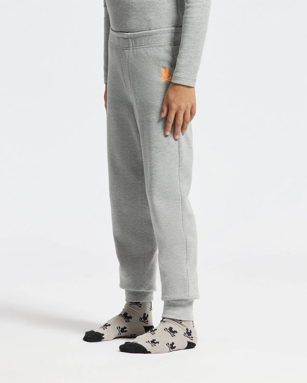 A person wearing Psycho Bunny's KIDS VAL WAFFLE PANT - B0P673E200 in light gray, matched with a coordinating long-sleeve shirt. They have one hand resting on their side. Gray socks featuring black patterns and black toe caps complete the look as they stand against a plain white background.