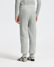 A rear view of a person wearing Psycho Bunny's KIDS VAL WAFFLE PANT - B0P673E200, styled in light gray with a matching top, is pictured. Their gray socks with black patterns add a touch of flair to the look. They stand comfortably against a plain white backdrop, hands relaxed by their sides.
