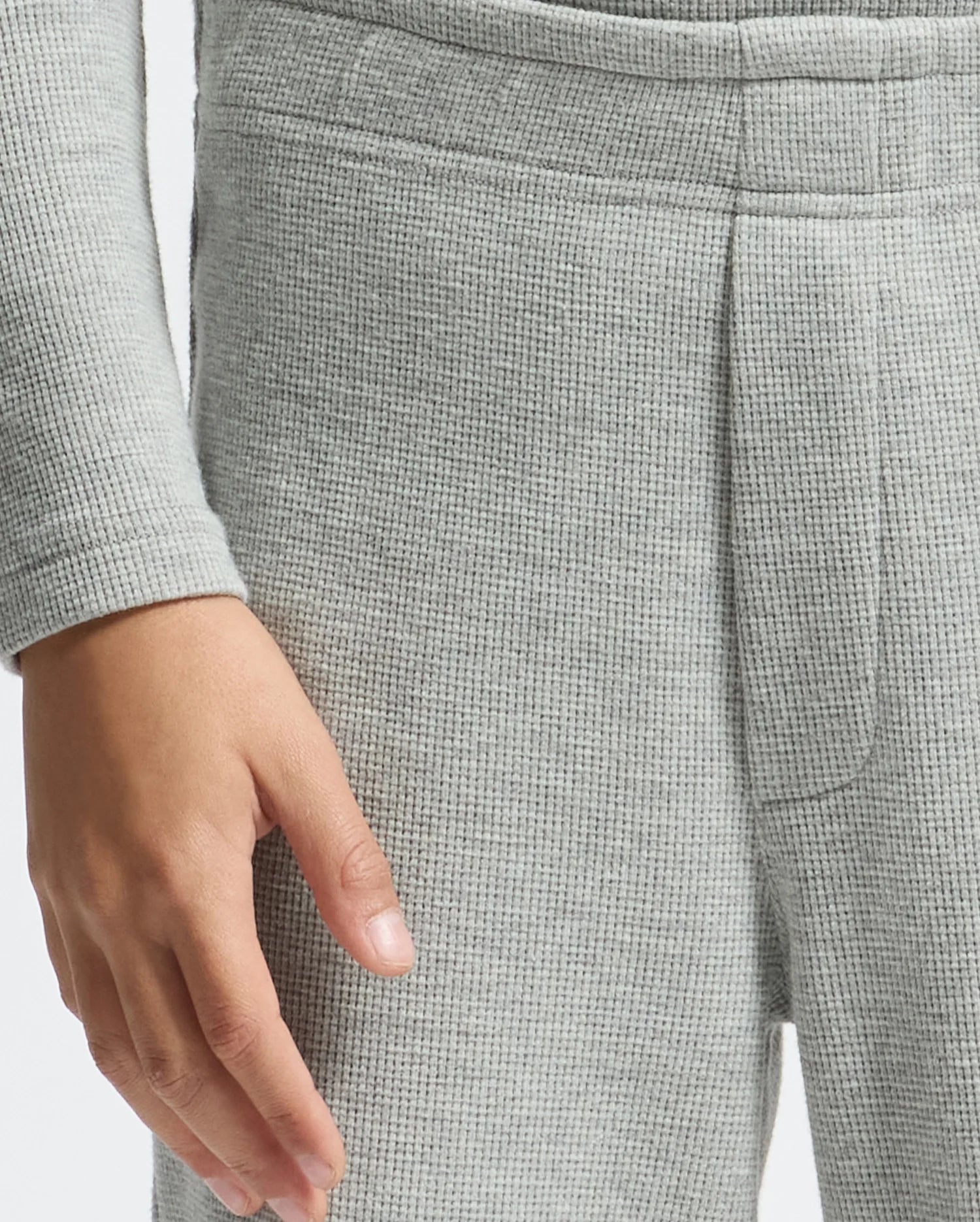 A person dressed in cozy waffle pants, specifically the KIDS VAL WAFFLE PANT - B0P673E200 by Psycho Bunny, has their right hand resting by their side. The soft, textured fabric highlights the hand and subtly draws attention to the details of both the sleeve and pants.