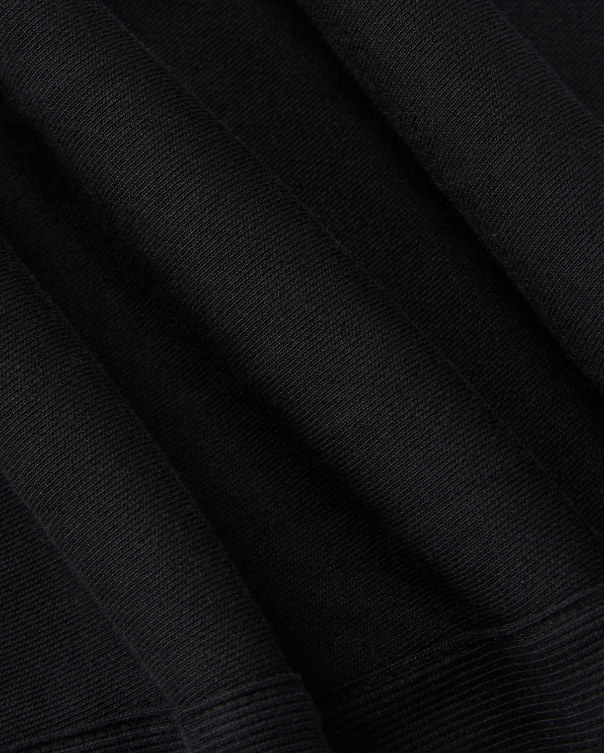 Close-up of the KIDS LEVY ESSENTIAL FLEECE SWEATPANT - B0P721D200 by Psycho Bunny. The black fabric has a ribbed texture and appears to have folds and creases, showcasing its thickness and material composition, much like cozy playtime pants. The texture suggests a soft and potentially warm fabric, ideal for clothing or upholstery needs.