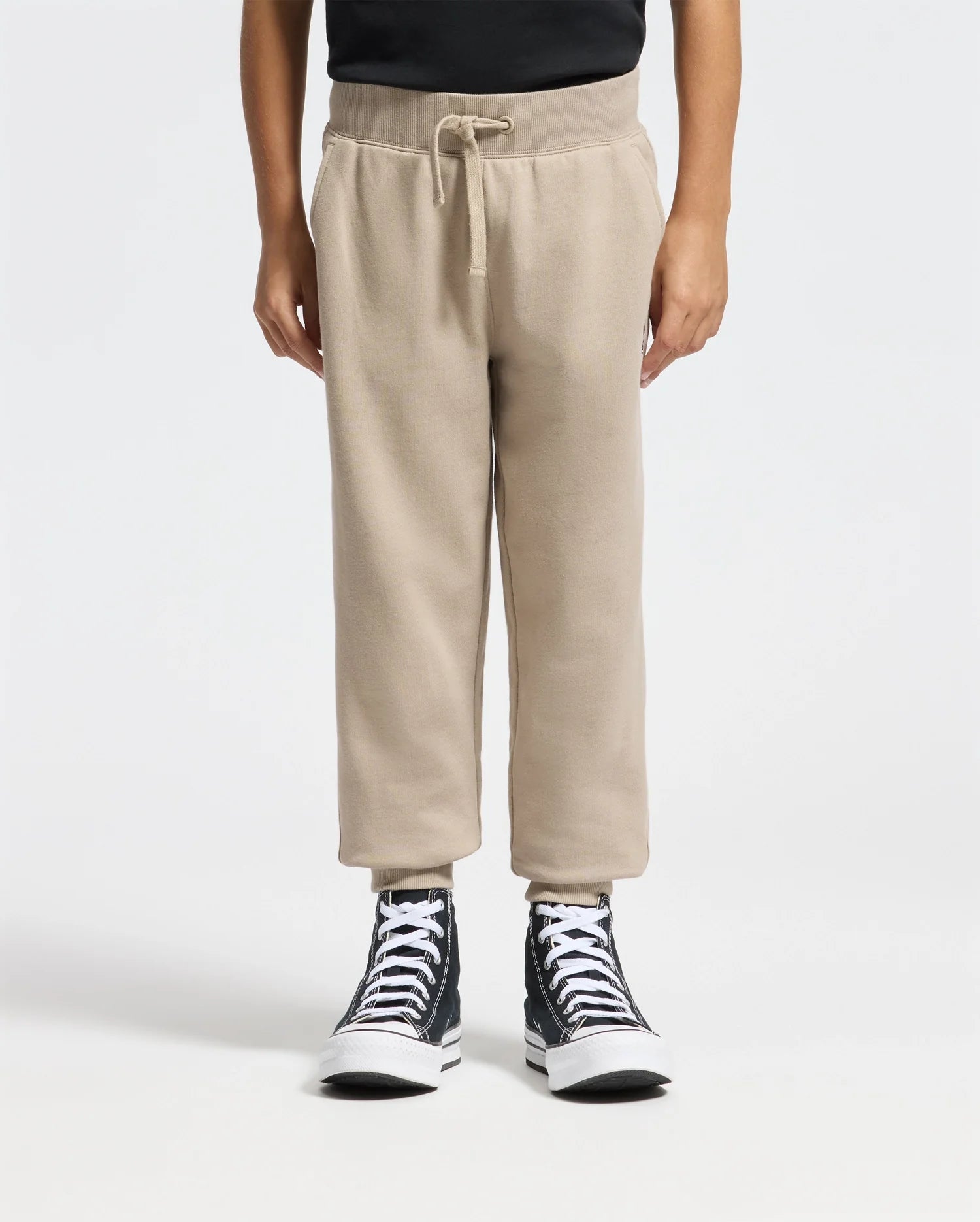 A person wearing a black shirt, the KIDS LEVY ESSENTIAL FLEECE SWEATPANT from Psycho Bunny featuring a cozy drawstring design, and black high-top sneakers stands against a plain white background, highlighting the comfort of their lower half.