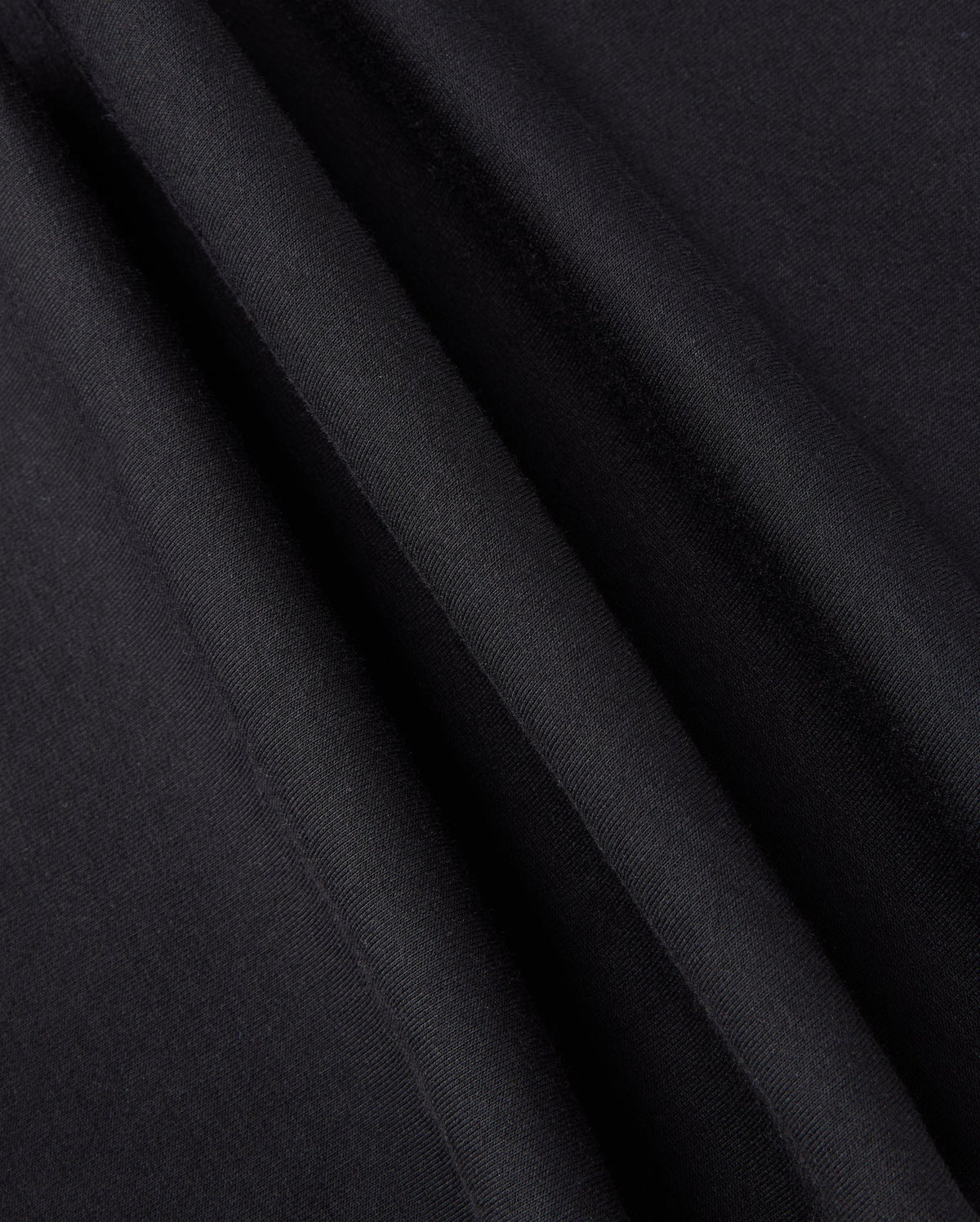 Close-up of black fabric with light reflecting off its smooth surface, creating subtle lines and textures. The material, perfect for the KIDS WALTER LIGHTWEIGHT SWEATPANT - B0P860D200 by Psycho Bunny, appears slightly folded or draped, showcasing its softness and sheen ideal for casual wear.