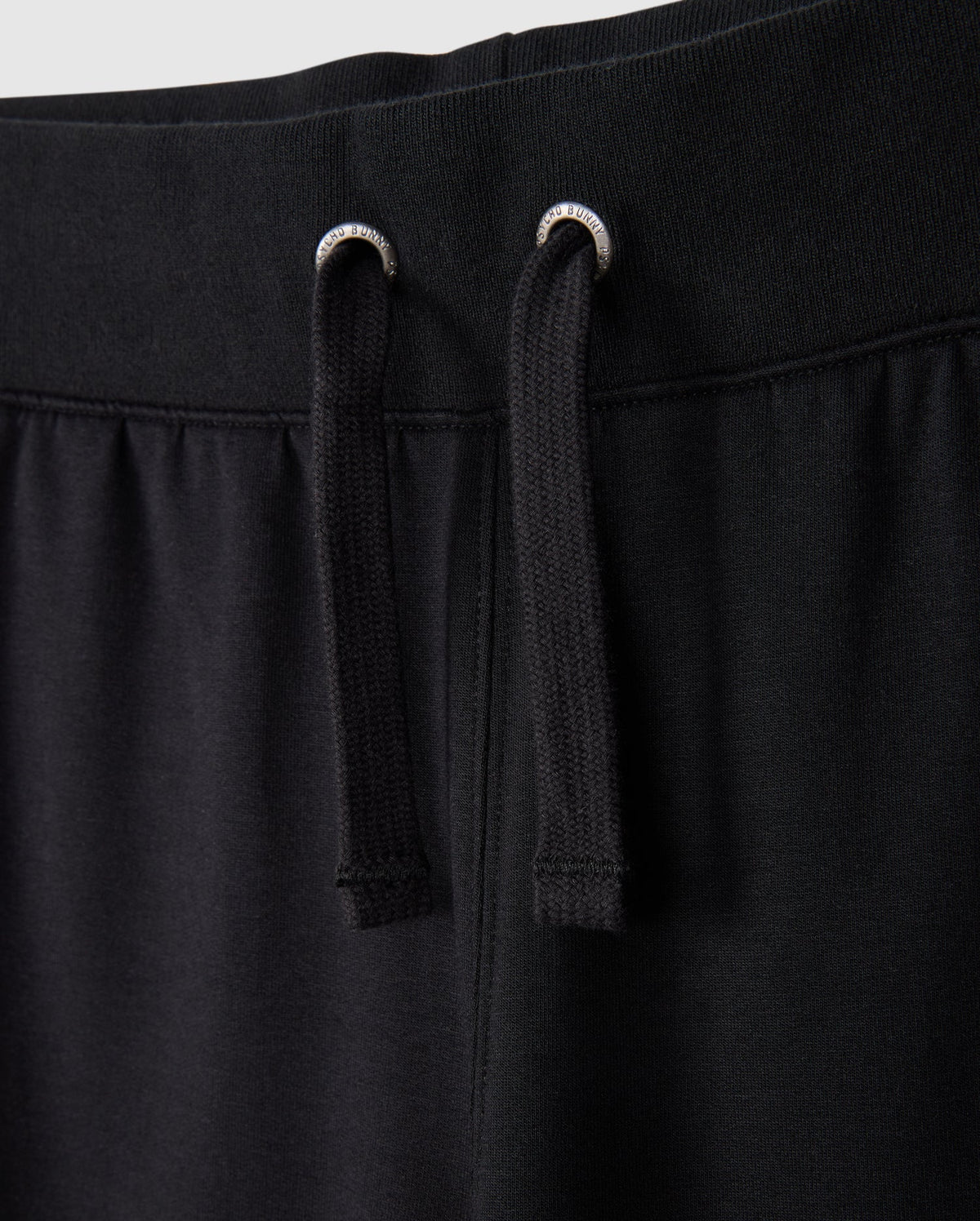 Close-up of the KIDS WALTER LIGHTWEIGHT SWEATPANT - B0P860D200 by Psycho Bunny. The image highlights the waistband and two black drawstrings with silver eyelets. The fabric appears soft and comfortable, showcasing the casual wear design and ensuring a breathable fit for all-day comfort.