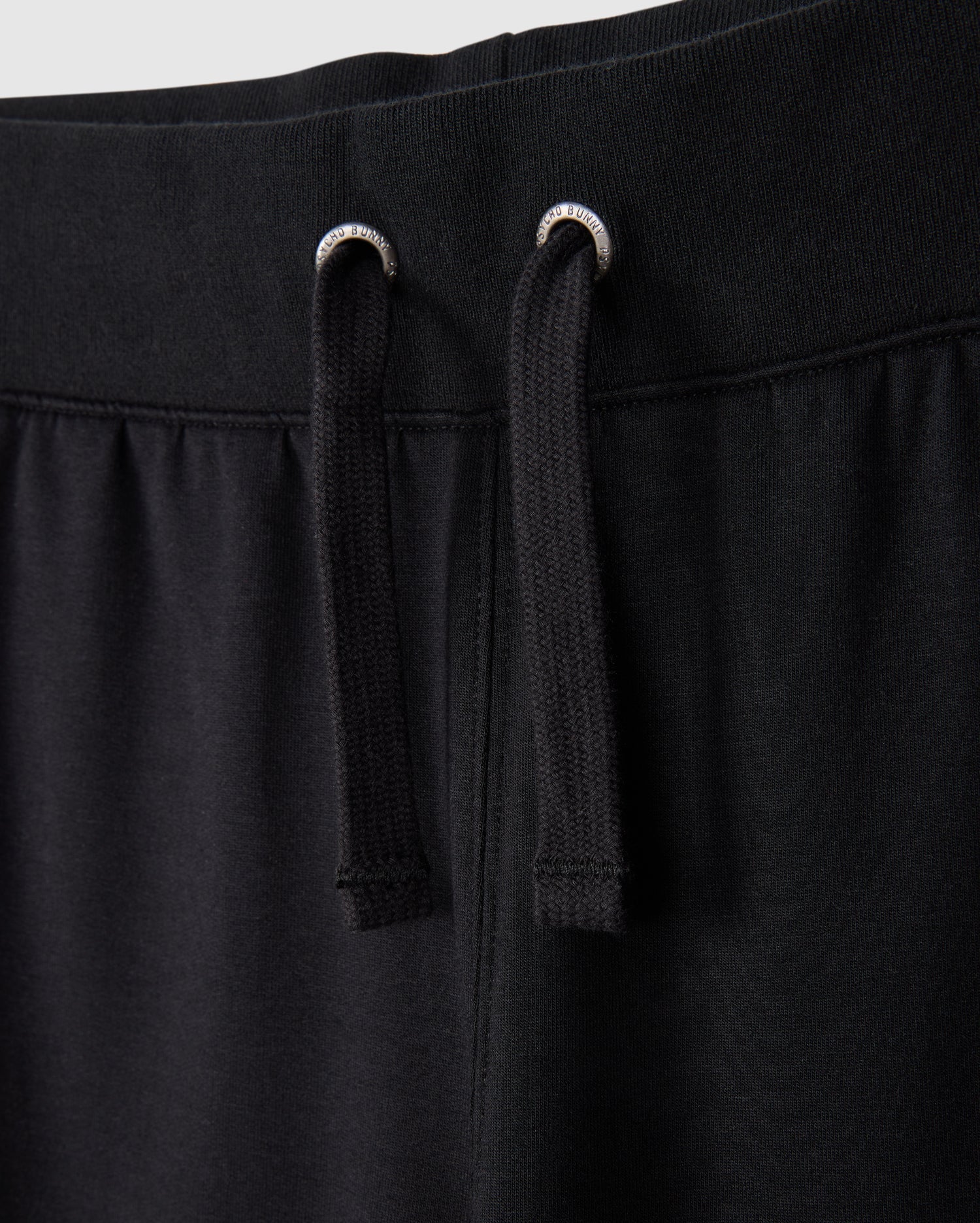 Close-up of the KIDS WALTER LIGHTWEIGHT SWEATPANT - B0P860D200 by Psycho Bunny. The image highlights the waistband and two black drawstrings with silver eyelets. The fabric appears soft and comfortable, showcasing the casual wear design and ensuring a breathable fit for all-day comfort.