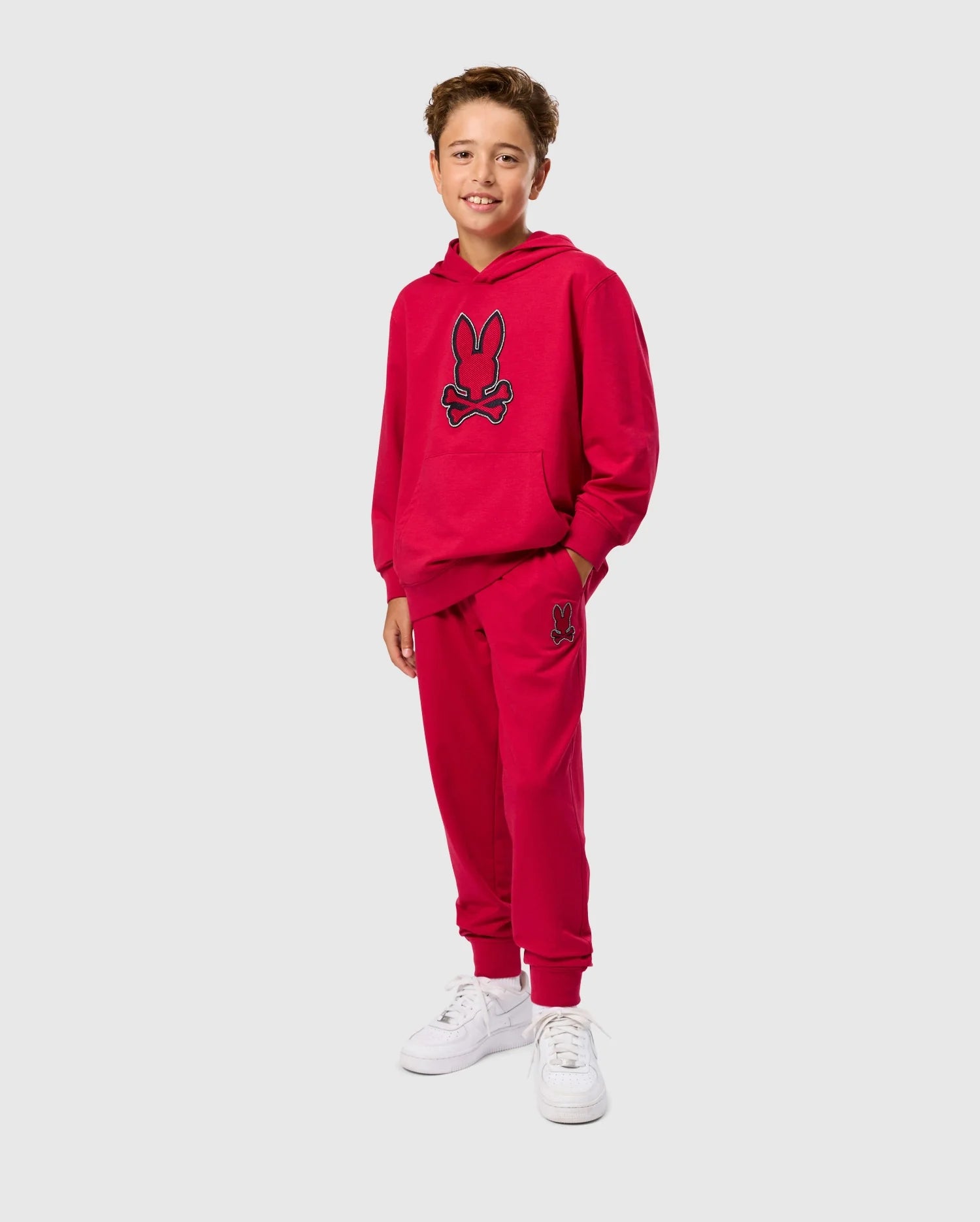 A boy in a red hoodie, paired with the KIDS WALTER LIGHTWEIGHT SWEATPANT by Psycho Bunny, epitomizes casual wear with a breathable fit for everyday comfort.