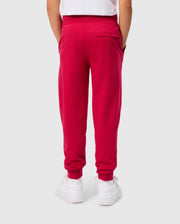 A child is seen from behind wearing the KIDS WALTER LIGHTWEIGHT SWEATPANT - B0P860D200 in a vibrant red color by Psycho Bunny, paired with a white shirt. The sweatpants feature two side pockets and one back pocket. White sneakers complete the outfit. The breathable fit of this casual wear contrasts nicely with the plain light gray background.