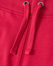 Close-up of the KIDS WALTER LIGHTWEIGHT SWEATPANT - B0P860D200 by Psycho Bunny in red, featuring drawstrings. The fabric appears soft and slightly textured, with two metal grommets through which the drawstrings are threaded. The seam is visible, indicating sturdy construction and ensuring a breathable fit ideal for casual wear.