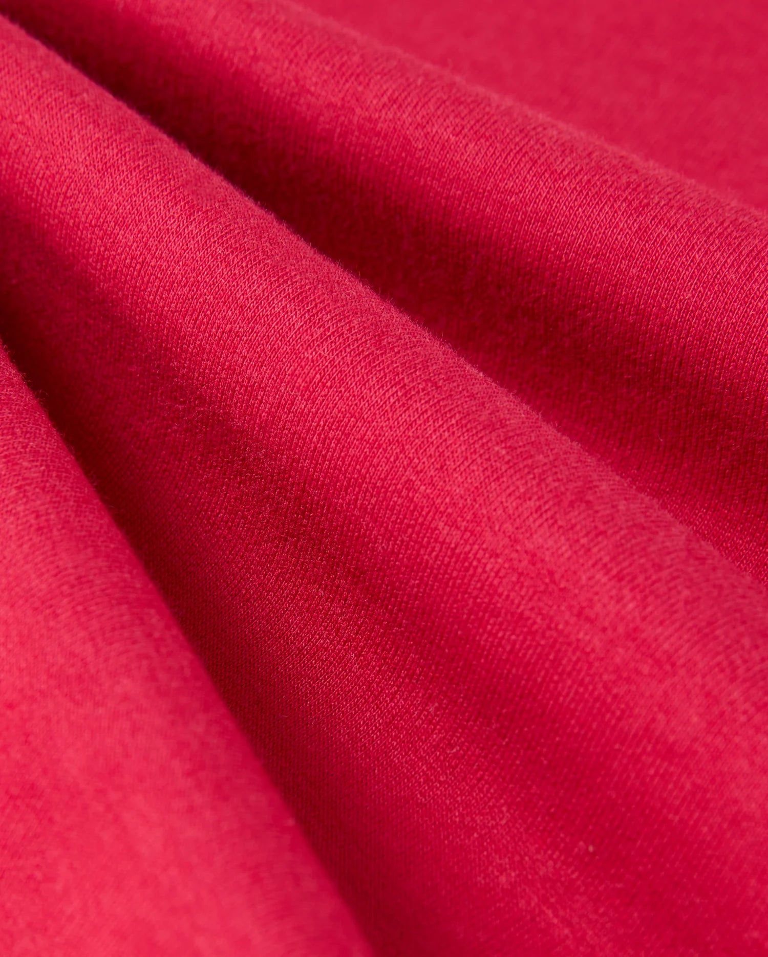 Close-up of the red fabric in the KIDS WALTER LIGHTWEIGHT SWEATPANT - B0P860D200 by Psycho Bunny. The texture appears soft and smooth, with even, consistent coloration. The fabric catches light subtly, highlighting its fine weave and slight sheen—perfect for a breathable fit in casual wear or lightweight sweatpants.