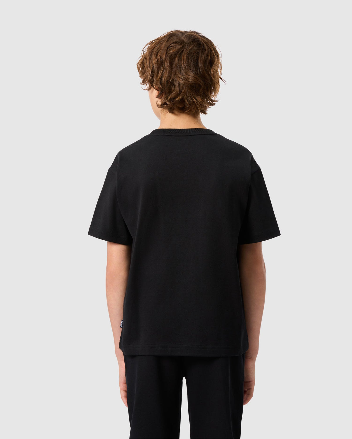 A person with curly brown hair, facing away from the camera, is wearing a plain black T-shirt and KIDS MONROE TWILL PATCH FLEECE SWEATPANT by Psycho Bunny in soft cotton fleece against a light gray background, highlighting subtle luxury finishes.