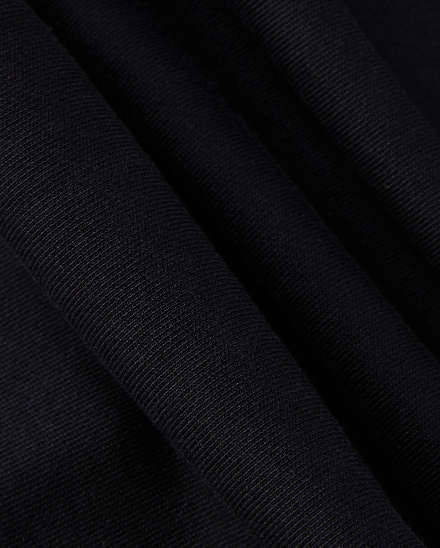 A close-up of the KIDS MONROE TWILL PATCH FLEECE SWEATPANT by Psycho Bunny showcases the black textured fabric with folds, highlighting its weave and subtle sheen akin to luxury finishes.