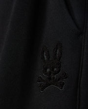 Close-up of the fabric from the KIDS PACIFIC CHENILLE JOGGER by Psycho Bunny, featuring an embroidered patch with a stylized black bunny head above crossed bones. This high-pile chenille logo patch adds a distinctive touch to any casual bottom or jogger pant.