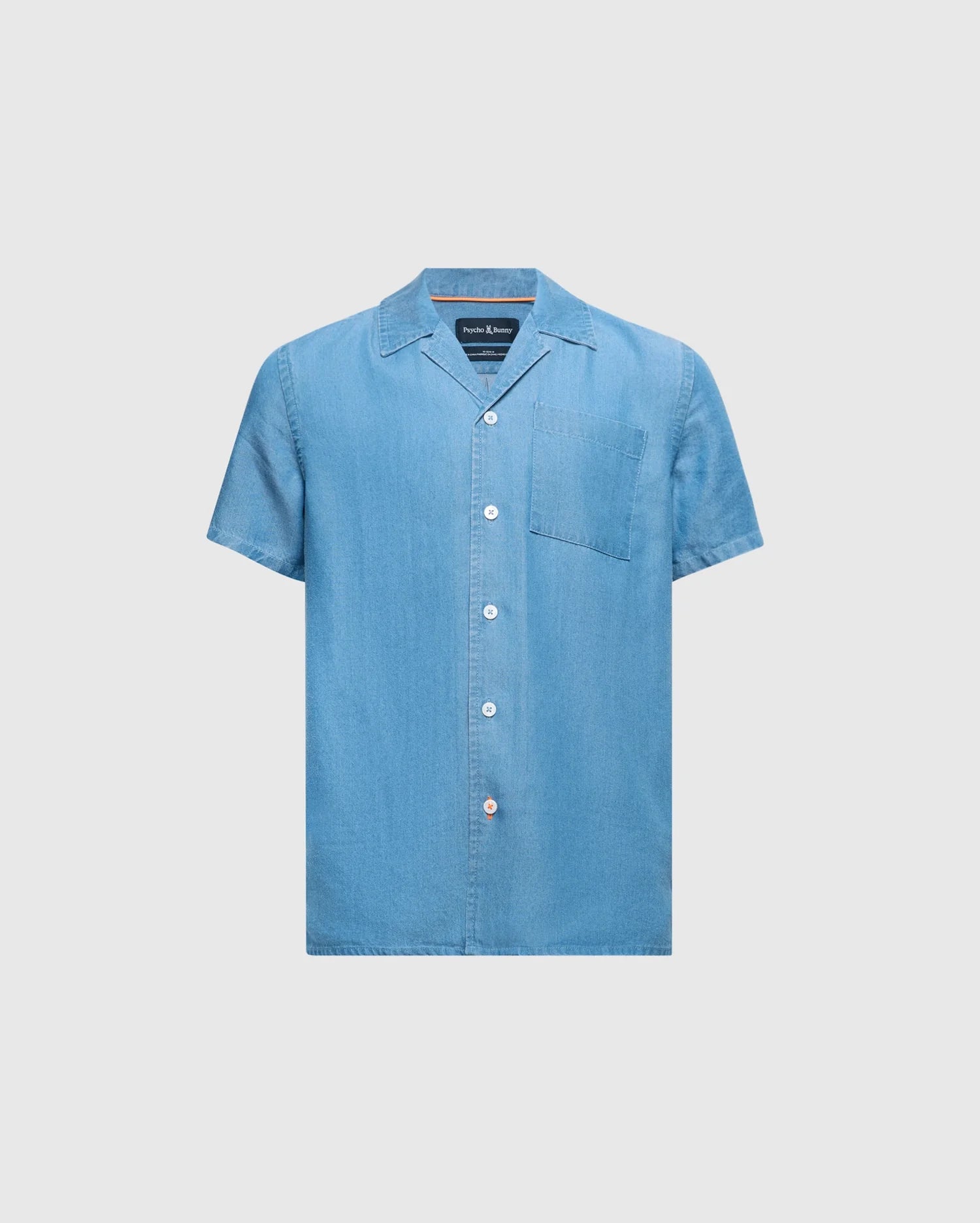 The KIDS KERVIN LIGHTWEIGHT DENIM WOVEN SHIRT by Psycho Bunny, in light blue with a front pocket and mother-of-pearl buttons, features a classic collar and casual style. Perfect for warm weather, it is displayed against a plain background. Product ID: B0Q467F200.