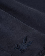 Close-up of Psycho Bunny kids' shorts made from dark KIDS WILLIS STRETCH TENCEL SHORT - B0R239Y1WB twill with a subtle, embroidered logo of a rabbit. The embroidery detail is in a slightly lighter shade of the same color as the fabric.
