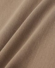 Close-up of a textured brown fabric with visible fine mesh-like patterns and slight creases. The surface, made from lightweight Pima cotton, showcases a detailed weave, offering material softness and flexibility—perfect for crafting stylish wardrobe staples like the KIDS STANFORD LIGHT PIQUE SWEATSHORT - B0R344B200 by Psycho Bunny.