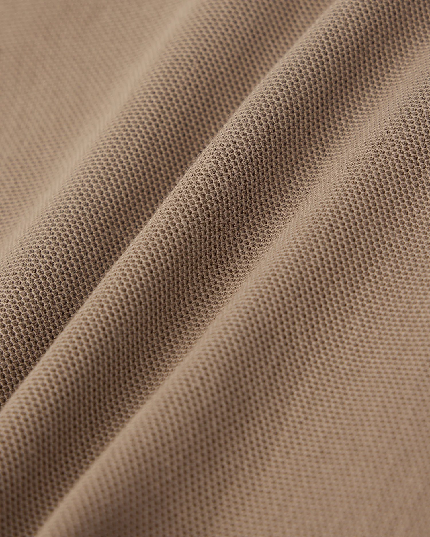 Close-up of a textured brown fabric with visible fine mesh-like patterns and slight creases. The surface, made from lightweight Pima cotton, showcases a detailed weave, offering material softness and flexibility—perfect for crafting stylish wardrobe staples like the KIDS STANFORD LIGHT PIQUE SWEATSHORT - B0R344B200 by Psycho Bunny.