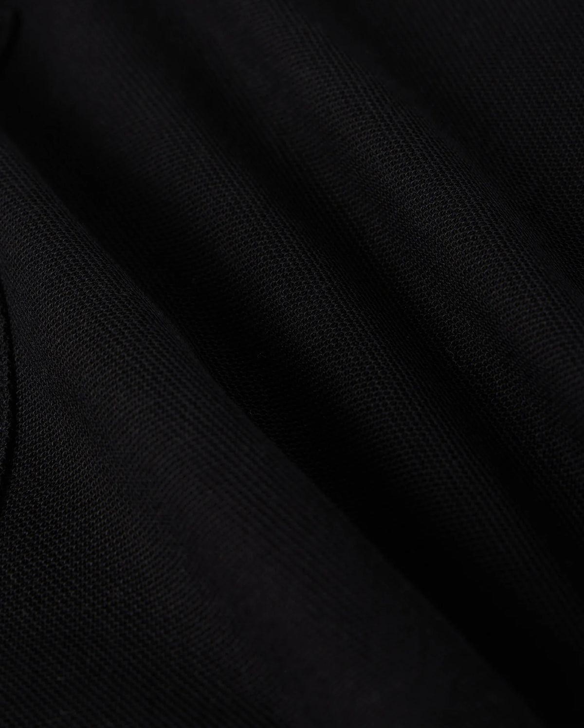 Close-up of a black fabric showing fine, detailed texture under light, creating slight shadows and highlights. The fabric appears smooth and slightly wrinkled, emphasizing its soft and elegant appearance—perfect for a stylish wardrobe staple like the KIDS STANFORD LIGHT PIQUE SWEATSHORT - B0R344B200 from Psycho Bunny.