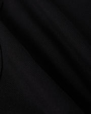 Close-up of a black fabric showing fine, detailed texture under light, creating slight shadows and highlights. The fabric appears smooth and slightly wrinkled, emphasizing its soft and elegant appearance—perfect for a stylish wardrobe staple like the KIDS STANFORD LIGHT PIQUE SWEATSHORT - B0R344B200 from Psycho Bunny.