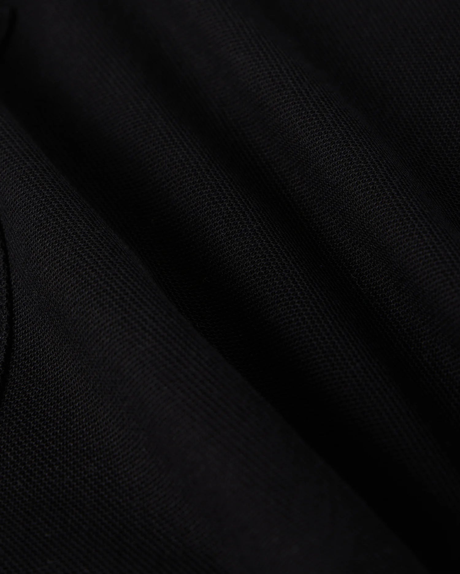 Close-up of a black fabric showing fine, detailed texture under light, creating slight shadows and highlights. The fabric appears smooth and slightly wrinkled, emphasizing its soft and elegant appearance—perfect for a stylish wardrobe staple like the KIDS STANFORD LIGHT PIQUE SWEATSHORT - B0R344B200 from Psycho Bunny.