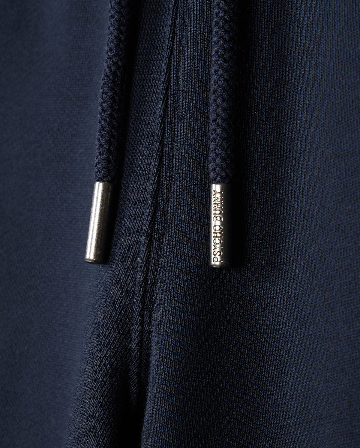 Close-up of dark blue fabric sweatshorts with navy drawstrings featuring "Psycho Bunny" engraved metal tips. This naturally breathable fleece from Psycho Bunny's KIDS LENOX SWEATSHORT - B0R377B200 collection is perfect for an active lifestyle.