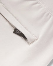 Close-up view of a beige micro French terry fabric with a metal zipper partially unzipped, showing a detailed floral pattern on a small fabric tag from Psycho Bunny's KIDS LIVINGSTON TERRY SWEATSHORT - B0R408B200.