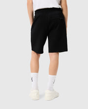 Rear view of a person wearing Psycho Bunny KIDS LYONS SWEATSHORT - B0R578C200, white socks with a logo near the top, and cream-colored sneakers, standing against a light background.