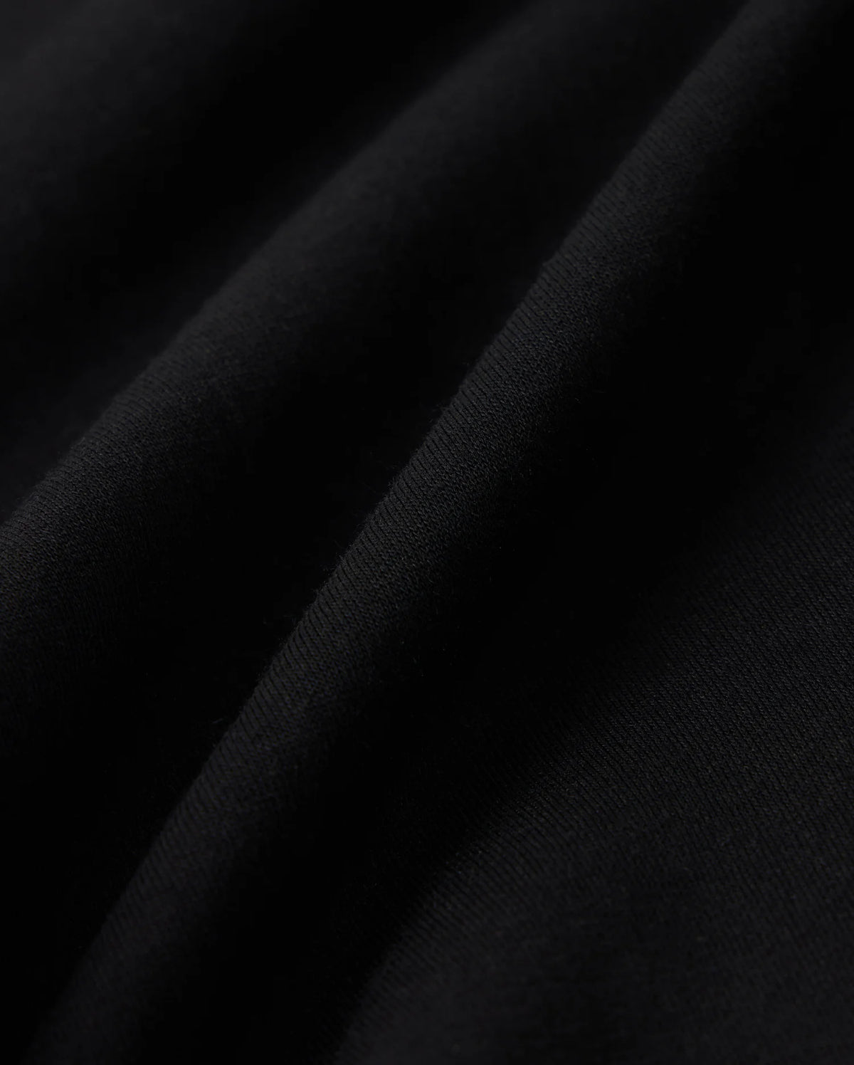 Close-up of black cotton blend fleece fabric with visible texture and soft folds. Light creates subtle highlights and shadows, emphasizing the Psycho Bunny KIDS LYONS SWEATSHORT - B0R578C200's fine details and quality.