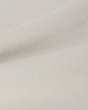 A close-up of a smooth, light beige fabric with a subtle texture. The material shows gentle folds, creating soft shadows and highlights across the surface. This lightweight, finely woven fabric is reminiscent of the soft stretch modal-cotton-blend jersey used in Psycho Bunny's KIDS LYONS SWEATSHORT - B0R578C200 for comfort and style.