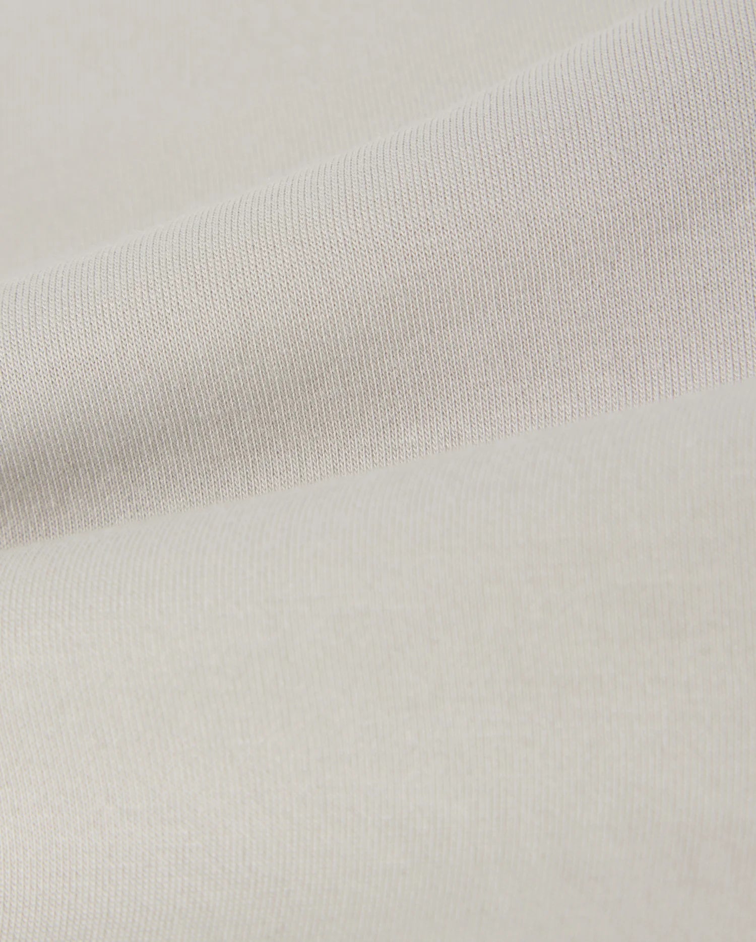 A close-up of a smooth, light beige fabric with a subtle texture. The material shows gentle folds, creating soft shadows and highlights across the surface. This lightweight, finely woven fabric is reminiscent of the soft stretch modal-cotton-blend jersey used in Psycho Bunny's KIDS LYONS SWEATSHORT - B0R578C200 for comfort and style.