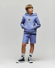 A boy wears Psycho Bunny's KIDS LEVANZO FRENCH TERRY SWEATSHORT (B0R578F200) and matching lavender hoodie with an embroidered Bunny skull logo, black high-top sneakers, and black-and-white socks, against a plain light background.
