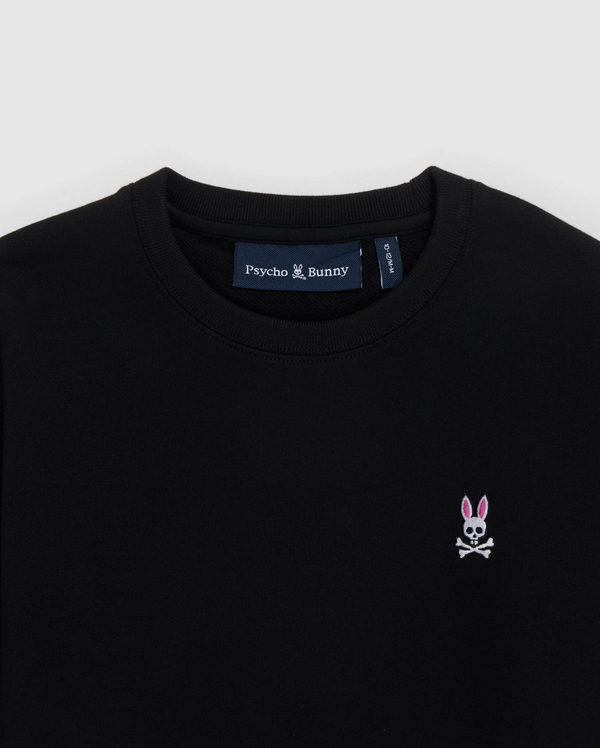 Close-up of a black KIDS FRENCH TERRY SWEATSHIRT - B0S830ARFT with a small embroidered Bunny logo on the chest and a blue label on the neckline reading "Psycho Bunny".