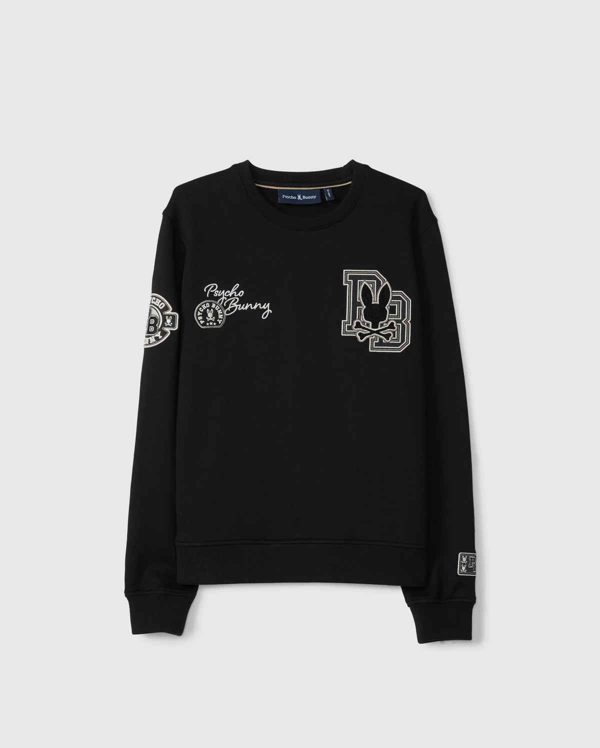 The KIDS ZACK VARSITY SWEATSHIRT by Psycho Bunny features chenille embroidery with a stylized letter “D” containing a rabbit, "Punk Bunny," and various decorative patches on the chest and sleeves. Its vintage-inspired logo is highlighted against the plain gray background of this black varsity sweatshirt.