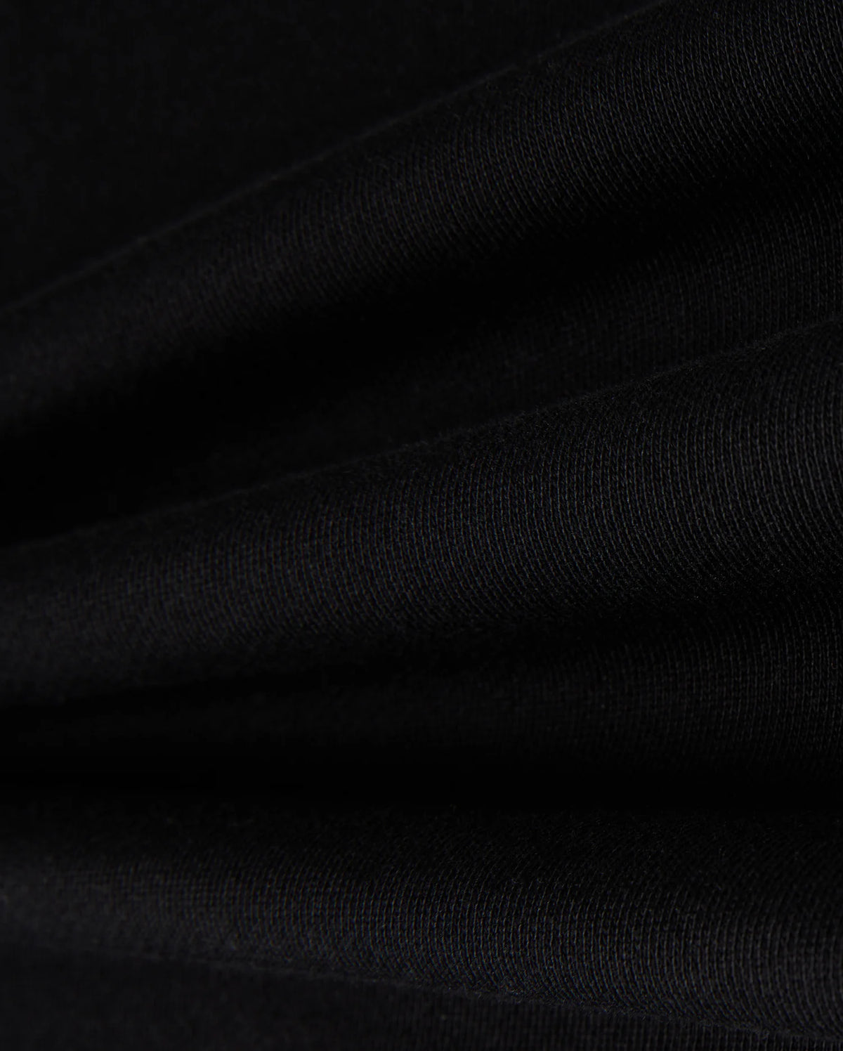 Close-up of Psycho Bunny's KIDS ZACK VARSITY SWEATSHIRT - B0S880D200 in black fabric, showcasing its visible texture with smooth folds that create parallel lines reminiscent of a varsity sweatshirt. The lighting accentuates the intricate weave, evoking the feel of chenille embroidery.
