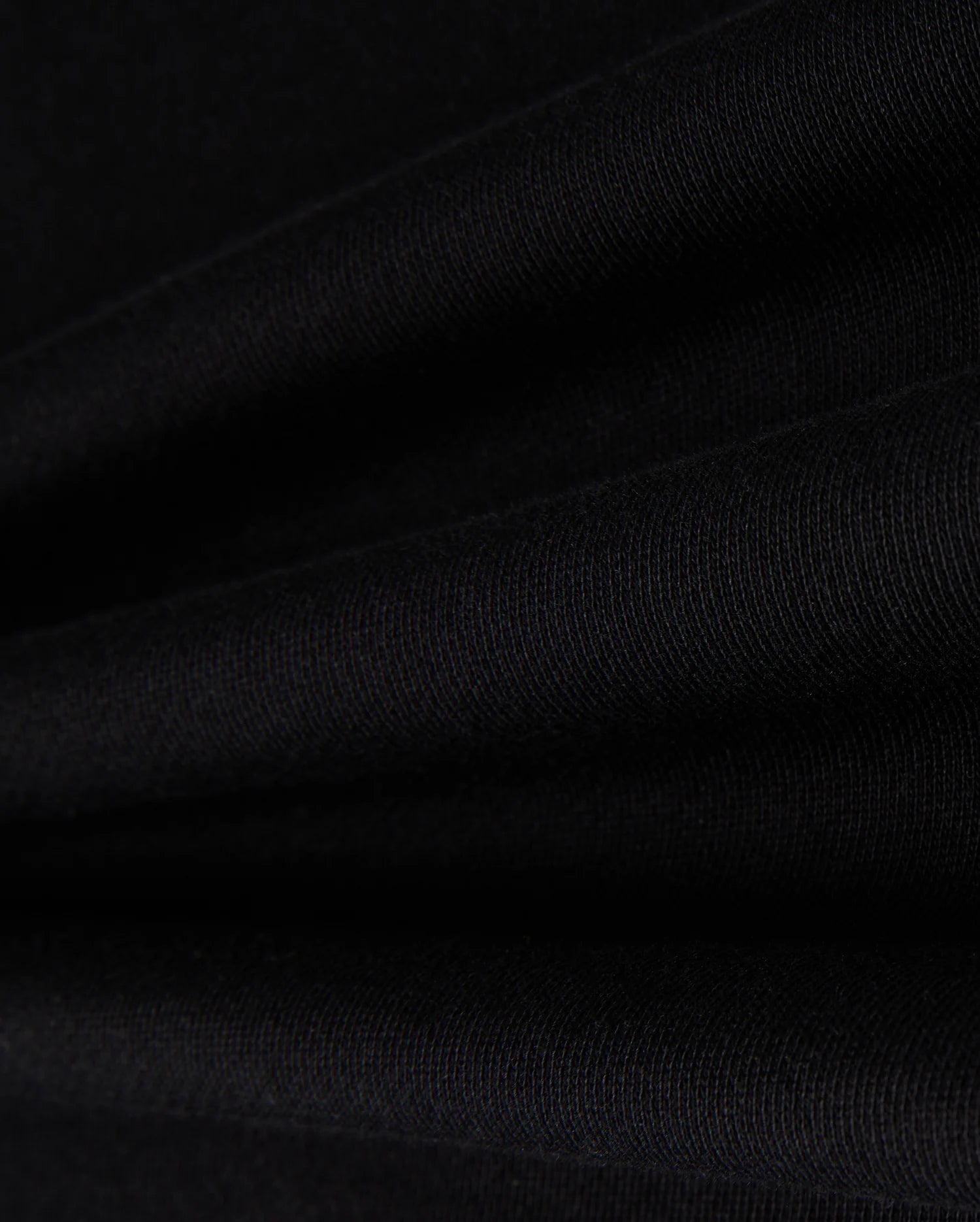 Close-up of Psycho Bunny's KIDS ZACK VARSITY SWEATSHIRT - B0S880D200 in black fabric, showcasing its visible texture with smooth folds that create parallel lines reminiscent of a varsity sweatshirt. The lighting accentuates the intricate weave, evoking the feel of chenille embroidery.