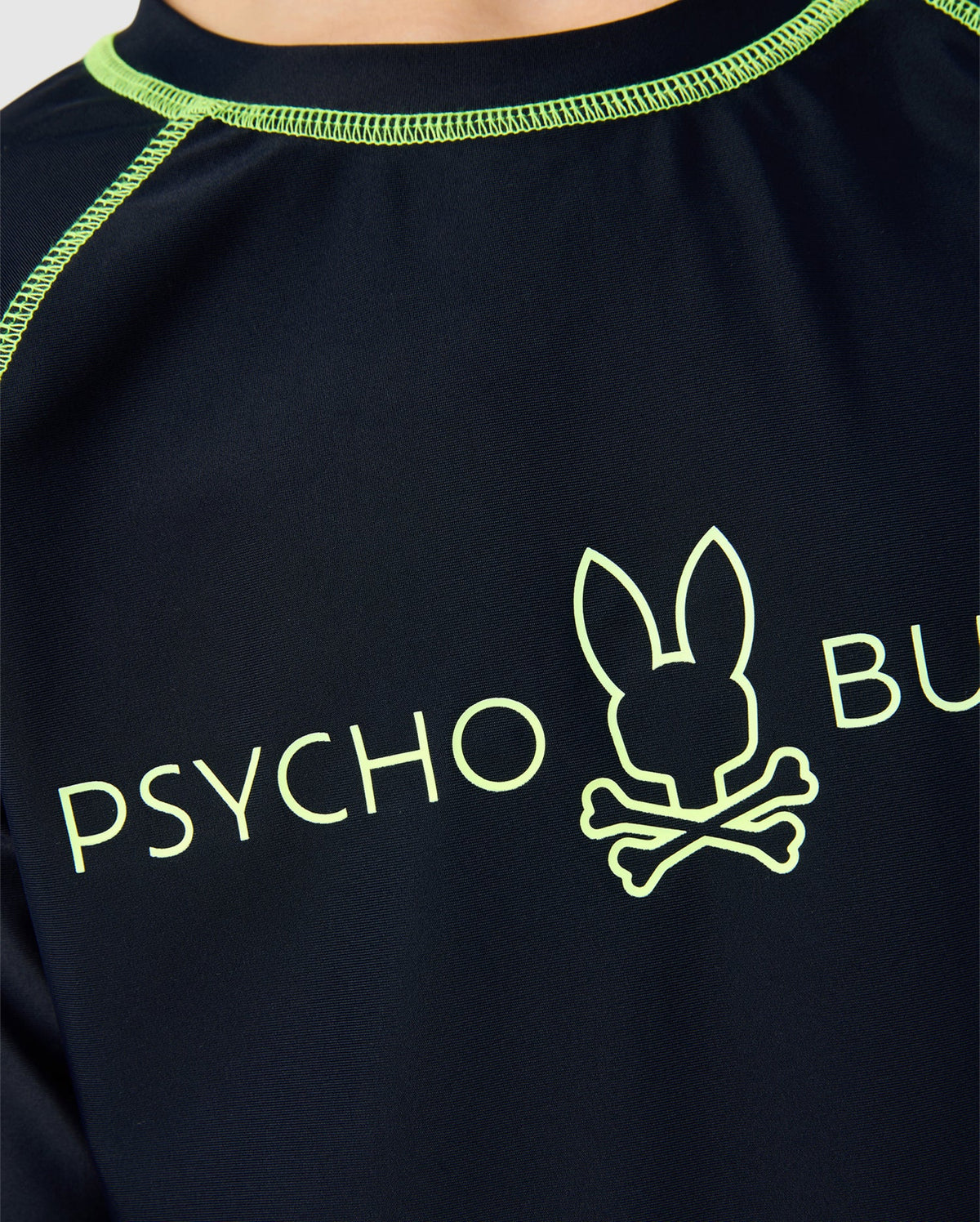 Close-up of the black Kids Long Sleeve Rash Guard B0T557C200 by Psycho Bunny, featuring green stitching, a stylized bunny head logo above crossbones, and "PSYCHO BUNNY" text in green. This quick-drying shirt offers UPF 50+ protection, ideal for sunny adventures.
