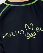 Close-up of the black Kids Long Sleeve Rash Guard B0T557C200 by Psycho Bunny, featuring green stitching, a stylized bunny head logo above crossbones, and "PSYCHO BUNNY" text in green. This quick-drying shirt offers UPF 50+ protection, ideal for sunny adventures.