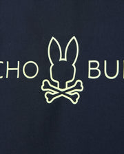 A yellow bunny head outline above crossed bones on a dark background offers quick-drying comfort. Partial letters "CHO" and "BU" are visible on this UPF 50+ Kids Long Sleeve Rash Guard from Psycho Bunny.