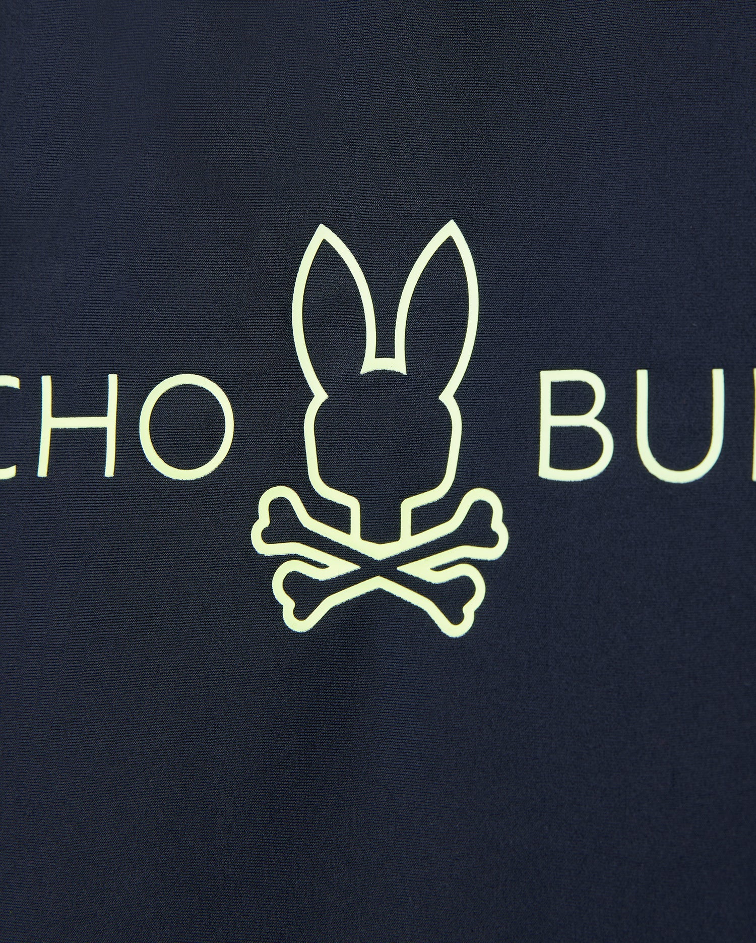 A yellow bunny head outline above crossed bones on a dark background offers quick-drying comfort. Partial letters "CHO" and "BU" are visible on this UPF 50+ Kids Long Sleeve Rash Guard from Psycho Bunny.