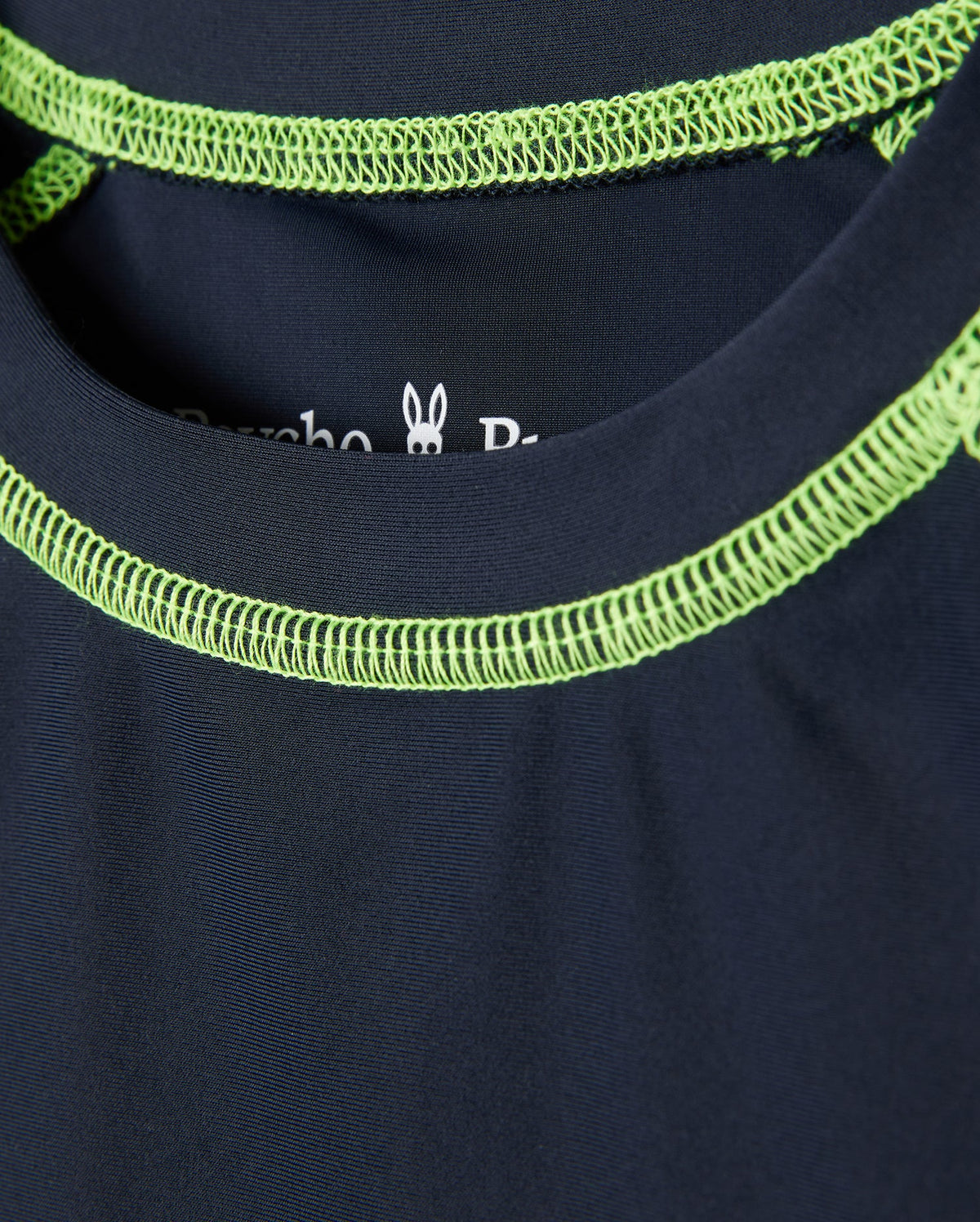 Close-up of a dark blue Psycho Bunny kids' long sleeve rash guard - B0T557C200, showcasing bright green neckline stitching and a small rabbit graphic inside the collar. It features quick-drying fabric and UPF 50+ protection for style and functionality.