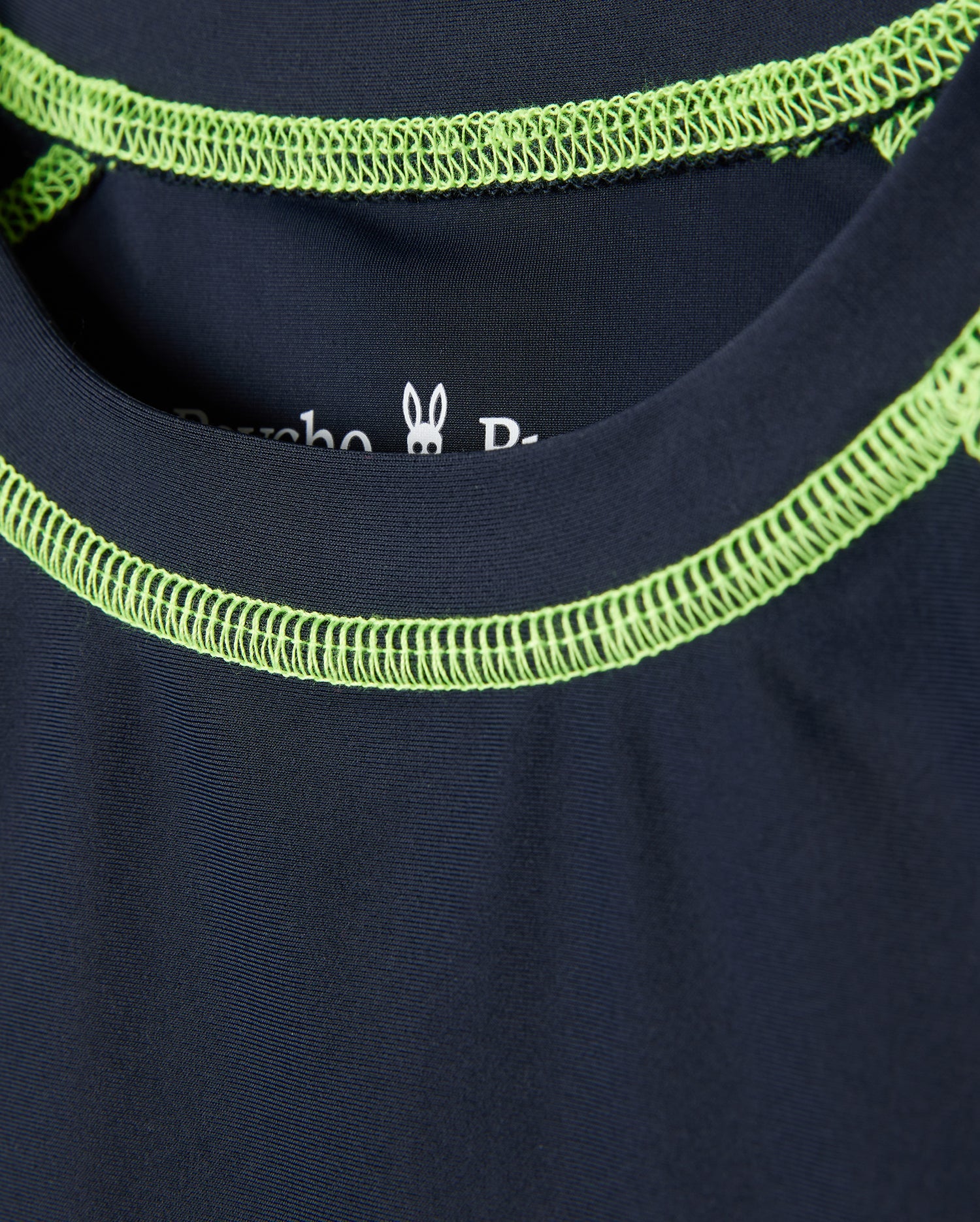 Close-up of a dark blue Psycho Bunny kids' long sleeve rash guard - B0T557C200, showcasing bright green neckline stitching and a small rabbit graphic inside the collar. It features quick-drying fabric and UPF 50+ protection for style and functionality.