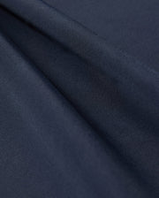 Close-up of folded, dark navy blue fabric from the Psycho Bunny KIDS LONG SLEEVE RASH GUARD - B0T557C200, showcasing its smooth texture and slight sheen. This fabric is ideal for a kids' rash guard with UPF 50+ protection, layered to create gentle folds and shadows.