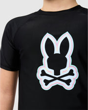 Close-up of a person wearing a Psycho Bunny Kids San Leon Anti-UV Rashguard with a neon outlined bunny skull and crossbones design on the back.