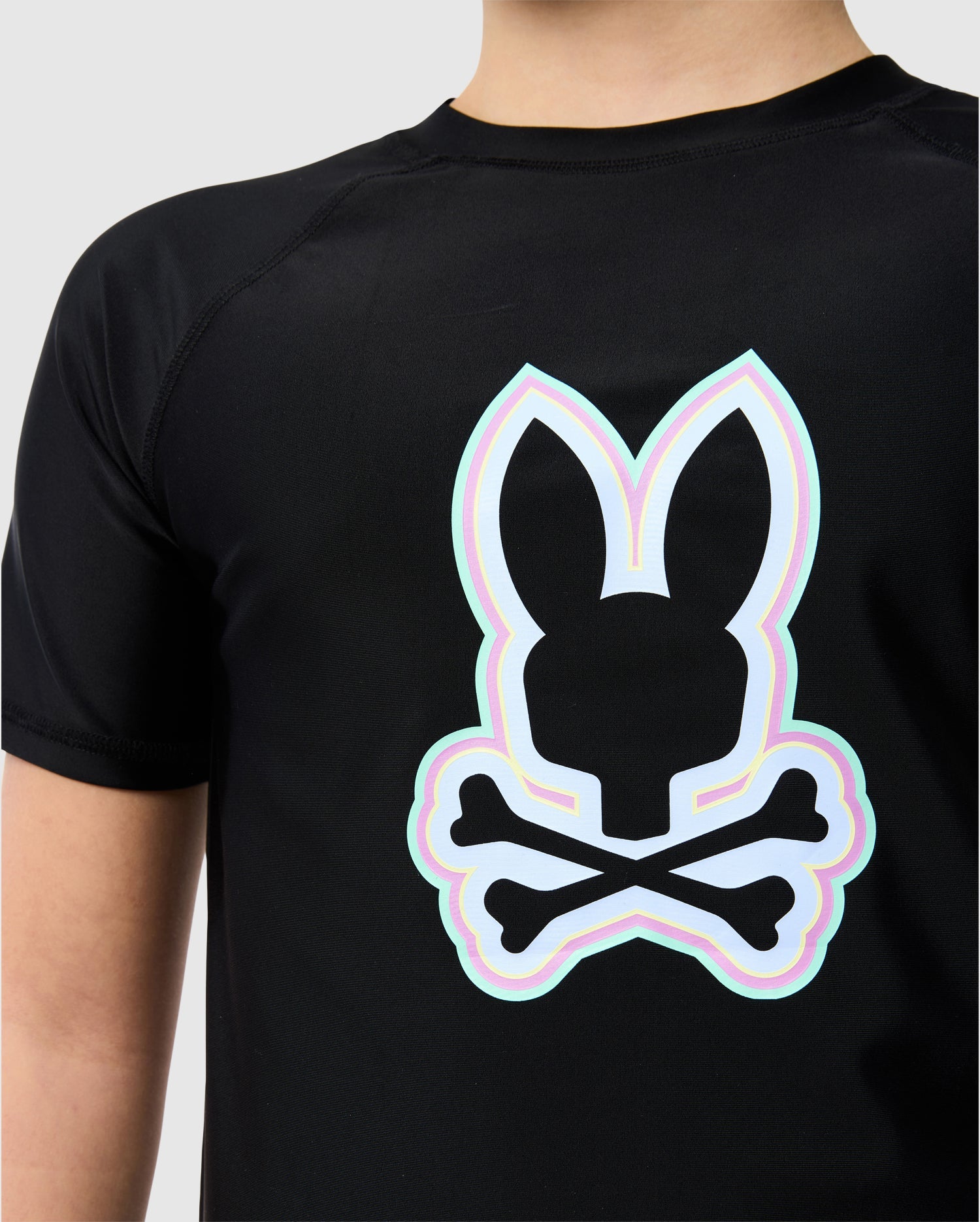 Close-up of a person wearing a Psycho Bunny Kids San Leon Anti-UV Rashguard with a neon outlined bunny skull and crossbones design on the back.