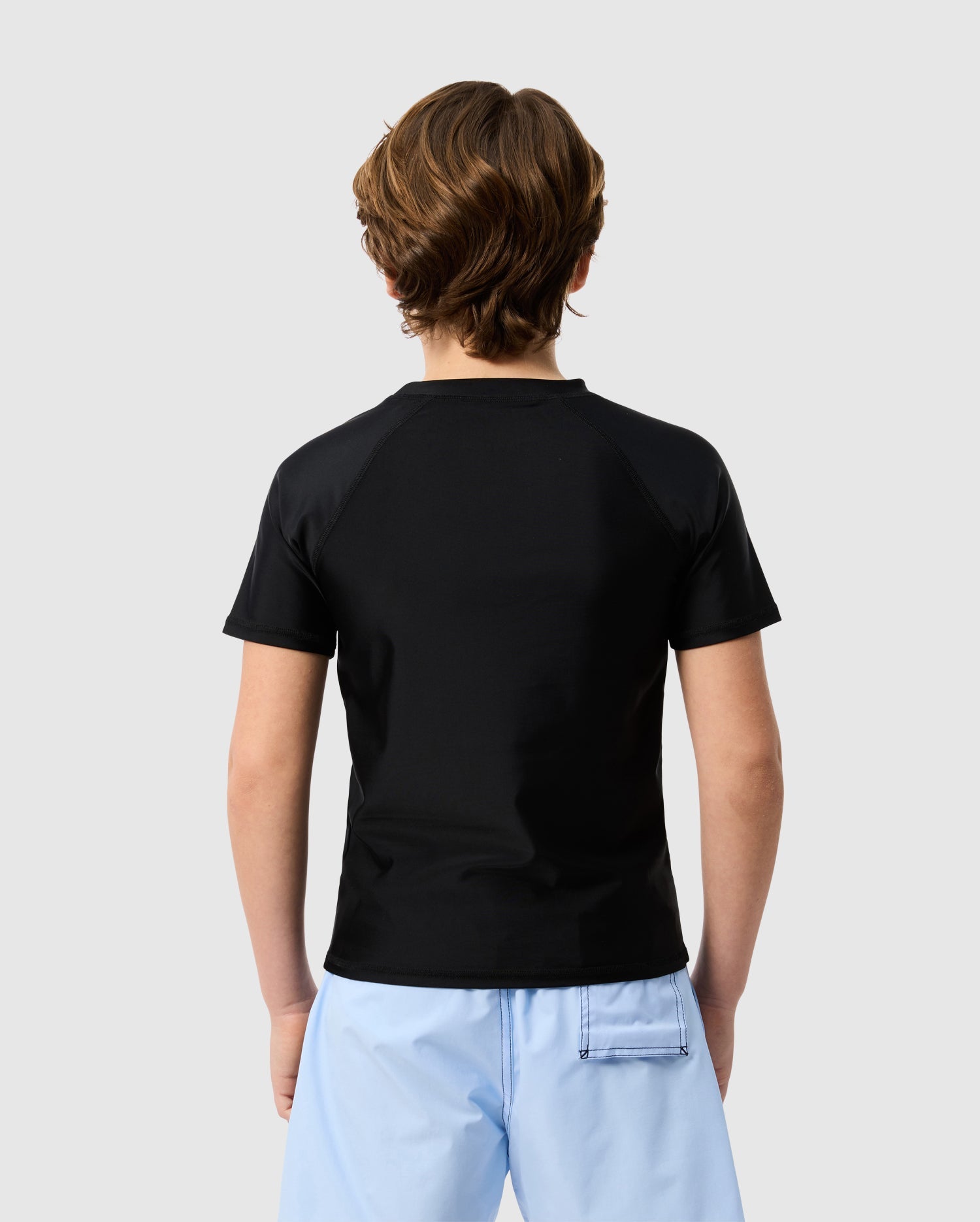 A person seen from behind wearing a Psycho Bunny KIDS SAN LEON ANTI-UV RASHGUARD - B0T645C200 in plain black and light blue shorts, standing against a plain white background.