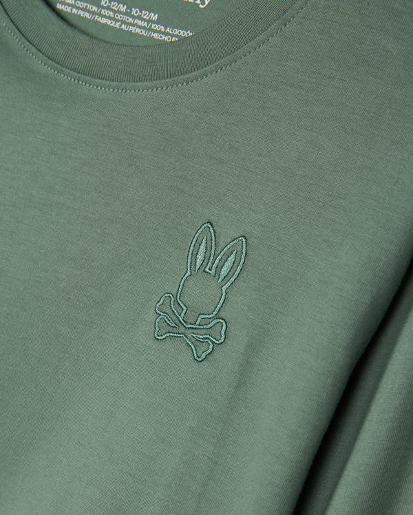 The KIDS ALBERTON LONG SLEEVE TEE (Model: B0T867D200) from Psycho Bunny is a green shirt made from soft Pima cotton, featuring a stitched emblem of rabbit ears and crossbones. Ideal for layering, the fabric label on the inside of the collar is partially visible.