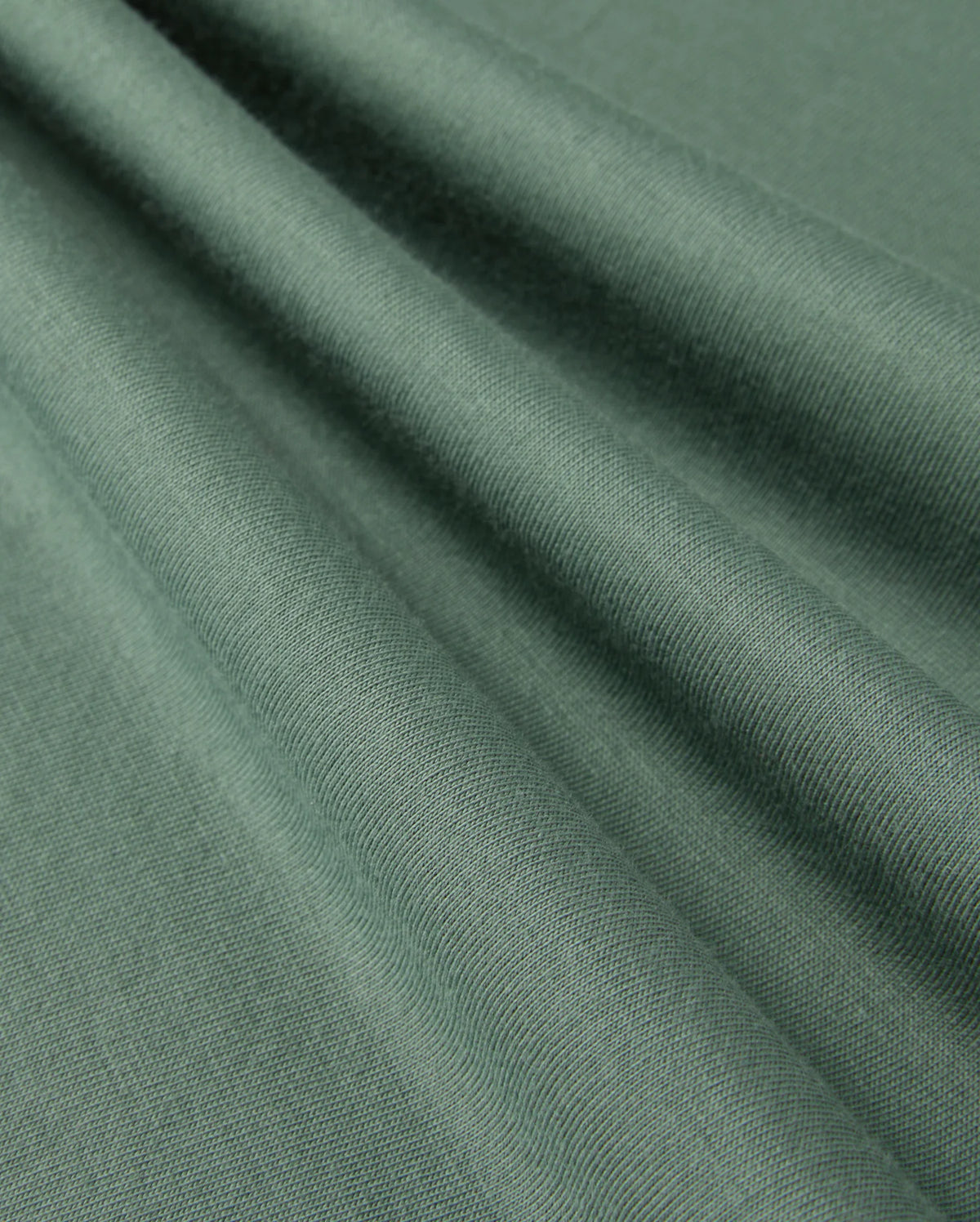 A close-up of folded Pima cotton fabric from the KIDS ALBERTON LONG SLEEVE TEE by Psycho Bunny, showcasing its smooth texture and subtle sheen. The fabric is draped in soft, diagonal folds, highlighting the material's flexibility and fine weave—perfect for creating a luxurious layering piece or a cozy long sleeve tee.